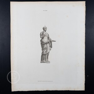 Op de afbeelding: Een antieke prent met een klassiek standbeeld van een vrouw in gedrapeerde kleding. De zwart-wit gravure toont de figuur staand op een sokkel, met één arm geheven en de andere uitgestrekt. De prent is op verouderd papier.