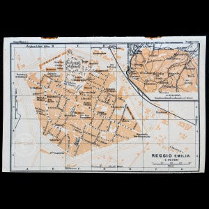 Puede incluir: Un mapa vintage de Reggio Emilia, Italia, con un sistema de cuadrícula y etiquetas para calles, puntos de referencia y áreas circundantes. El mapa está impreso en tinta negra y marrón sobre papel blanco.