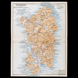 Könnte beinhalten: Eine historische Karte von Sardinien auf cremefarbenem Papier. Die Insel ist in hellem Orange gehalten, umgeben von blauem Wasser. Schwarze Linien markieren Straßen und Eisenbahnen, während Texte die Städte, Kaps und Golfregionen auf Italienisch benennen.