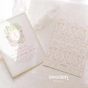May include: Two invitations for a second birthday party. The front of the invitation has a floral wreath design with the letter "A" in the center. The back of the invitation has a repeating pattern. The text on the invitation reads "The Two Two".