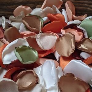 May include: A pile of silk rose petals in various colors, including white, peach, orange, brown, and green. The petals are arranged in a random pattern and are perfect for wedding decorations or other special events.