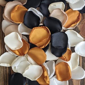 May include: A pile of fabric flower petals in black, white, and gold. The petals are made of satin and are arranged in a random pattern.