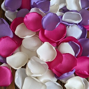 Pode incluir: Um monte de pétalas de flores de seda em branco, roxo e rosa. As pétalas estão dispostas em um padrão aleatório e são perfeitas para decorações de casamento ou outros eventos especiais.
