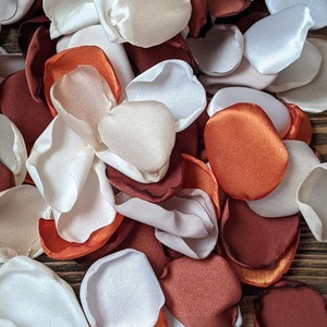 Op de afbeelding: Een stapel witte, ivoor en gebrande oranje zijden rozenblaadjes. De blaadjes zijn in een willekeurig patroon gerangschikt en zijn perfect voor bruiloftsdecoraties of andere speciale gelegenheden.