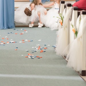 May include: White aisle runner with white tulle bows and orange flowers. Scattered blue, white, and orange flower petals on the floor.