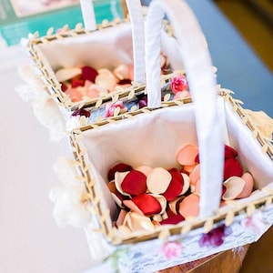May include: Two white baskets with lace trim and white ribbon handles filled with pink and red flower petals.