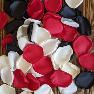 May include: A pile of red, white, and black silk rose petals. The petals are scattered on a wooden surface.