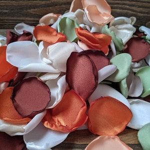 Puede incluir: Un montón de pétalos de rosa de tela en varios colores, incluyendo blanco, melocotón, verde salvia, naranja quemado y óxido.