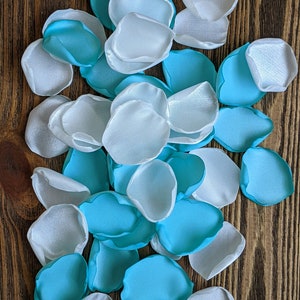 May include: A pile of teal and white silk rose petals. The petals are scattered on a wooden surface.
