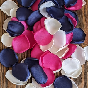May include: A collection of silk flower petals in navy blue, white, and fuchsia pink. The petals are arranged in a pile on a wooden surface.