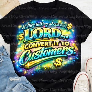 Pode incluir: T-shirt preto com o texto "If they talking about me, Lord... Convert it to Customers." O design apresenta detalhes coloridos e brilhantes e símbolos de dólar. A camisa é combinada com jeans azul e tênis brancos.