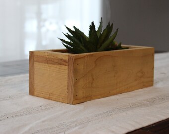 May include: A natural wood planter box with a succulent plant inside. The planter is made of unfinished wood and has a rectangular shape.
