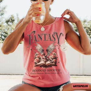 K&ouml;nnte beinhalten: Ein rosafarbenes Tanktop mit einer Grafik eines Drachen und eines Buches. Der Text auf dem Shirt lautet "Fantasy Readers Society Castles, Dragons, Wizards, Heroic Quests".