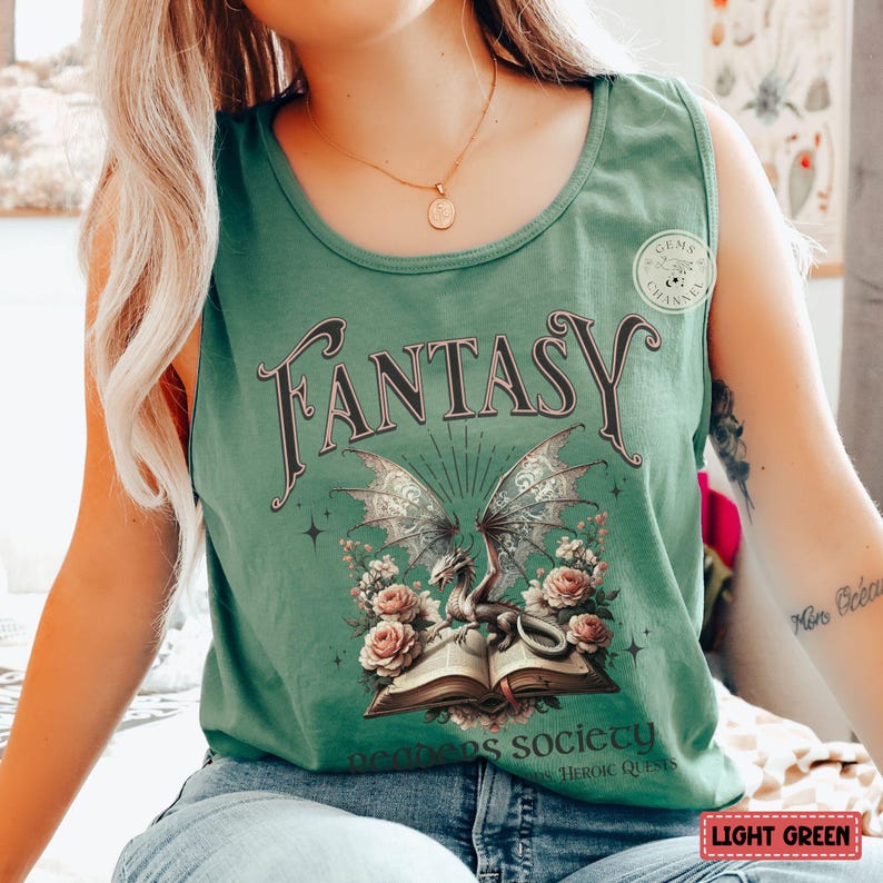 K&ouml;nnte beinhalten: Ein hellgr&uuml;nes Tanktop mit einem grafischen Druck eines Drachen, der ein offenes Buch h&auml;lt. Der Text "Fantasy" ist in Schwarz &uuml;ber dem Drachen gedruckt. Der Text "Where dreams society" ist in Schwarz unter dem Drachen gedruckt.
