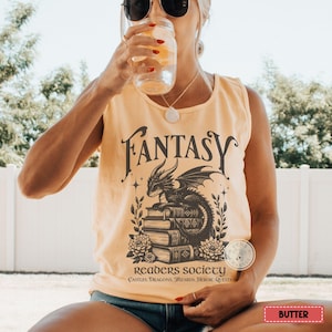 May include: A yellow tank top with a black graphic of a dragon sitting on a stack of books. The text "Fantasy Readers Society" is printed below the dragon. The text "Castles, Dragons, Wizards, Heroic Quests" is printed below the society name.