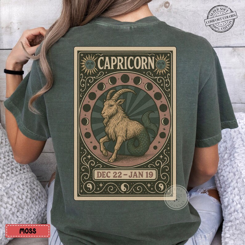 Puede incluir: Una camiseta verde musgo con un dise&ntilde;o del zodiaco Capricornio. El dise&ntilde;o incluye una ilustraci&oacute;n h&iacute;brida de cabra-pez, la palabra "CAPRICORNIO" y las fechas "22 DIC - 19 ENE". La camiseta tiene un aspecto vintage y desgastado.