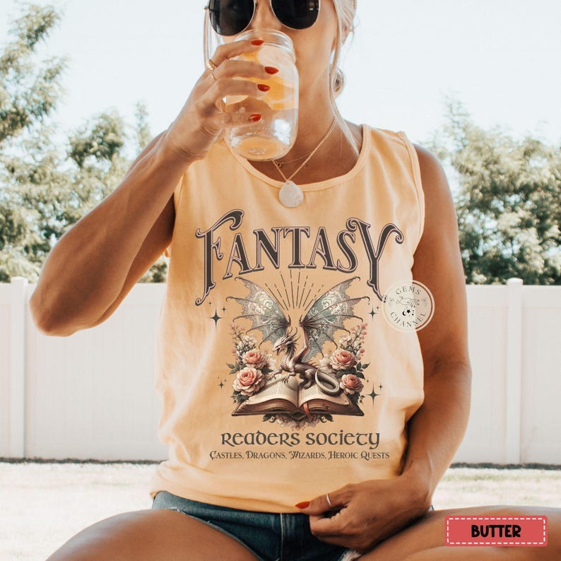 K&ouml;nnte beinhalten: Ein gelbes Tanktop mit einer Grafik eines Drachen und eines Buches. Der Text auf dem Shirt lautet "Fantasy Readers Society Castles, Dragons, Wizards, Heroic Quests".