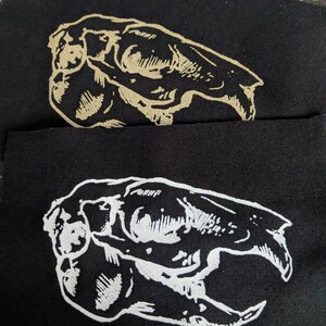 Könnte beinhalten: Zwei schwarze Stoffpatches mit einer weißen Umrandung eines Tierschädels. Der Schädel ist nach links gerichtet und hat ein detailliertes Design.