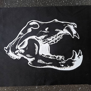 May include: A white silhouette of an animal skull with an open jaw on a black background.