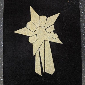 Può includere: Una stella dorata con una coda, su uno sfondo di tessuto nero.