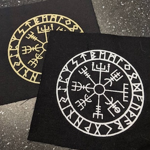 May include: Two black fabric patches with a white and gold compass design. The compass features a circle with runes and symbols around the edge. The compass is surrounded by a circle with the words "Vegvisir" and "Aett" in runes.