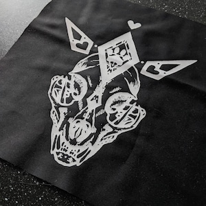May include: A black fabric patch with a white design of a skull with a diamond shape above it. The diamond has a paw print inside and a heart above it. There are two white triangles with hearts on each side of the diamond.