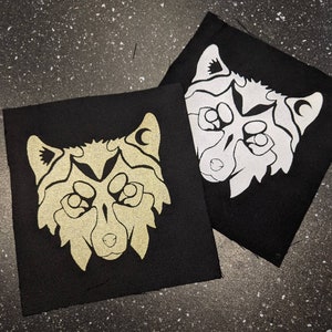 May include: Two black fabric patches featuring a white wolf design. The wolf has a crescent moon on its forehead and a stylised design around its eyes. The patches are of different sizes.