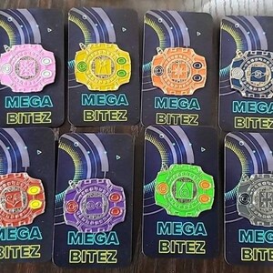 May include: Eight colorful enamel pins featuring a circular design with a central symbol and the text "MEGA BITEZ". The pins are arranged in two rows of four, with each pin on a separate card.