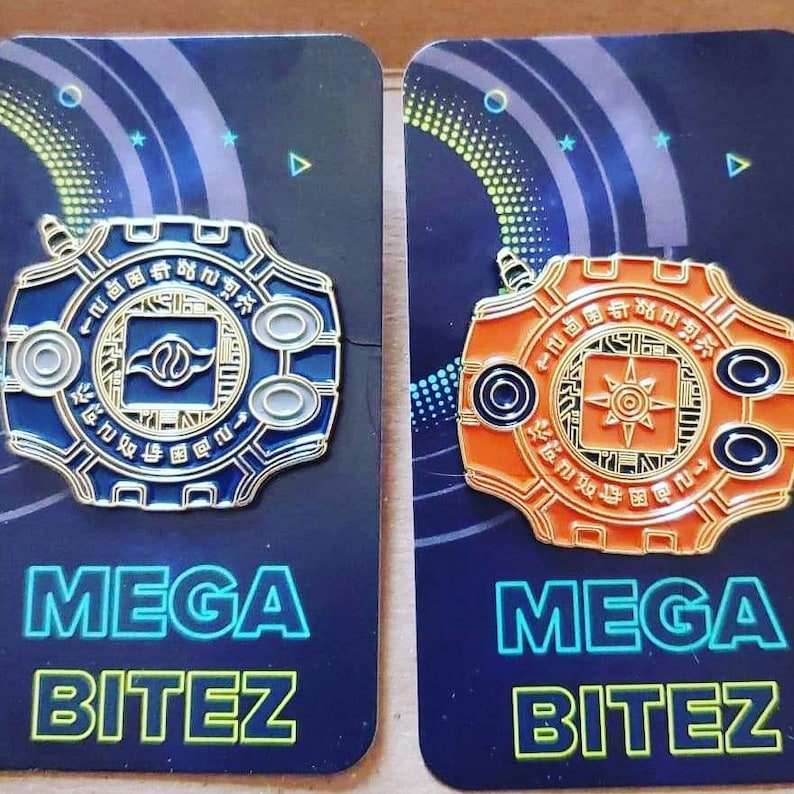 May include: Two enamel pins featuring Digimon characters. The pins are gold with blue and orange accents. The text "MEGA BITEZ" is printed on the bottom of each pin.