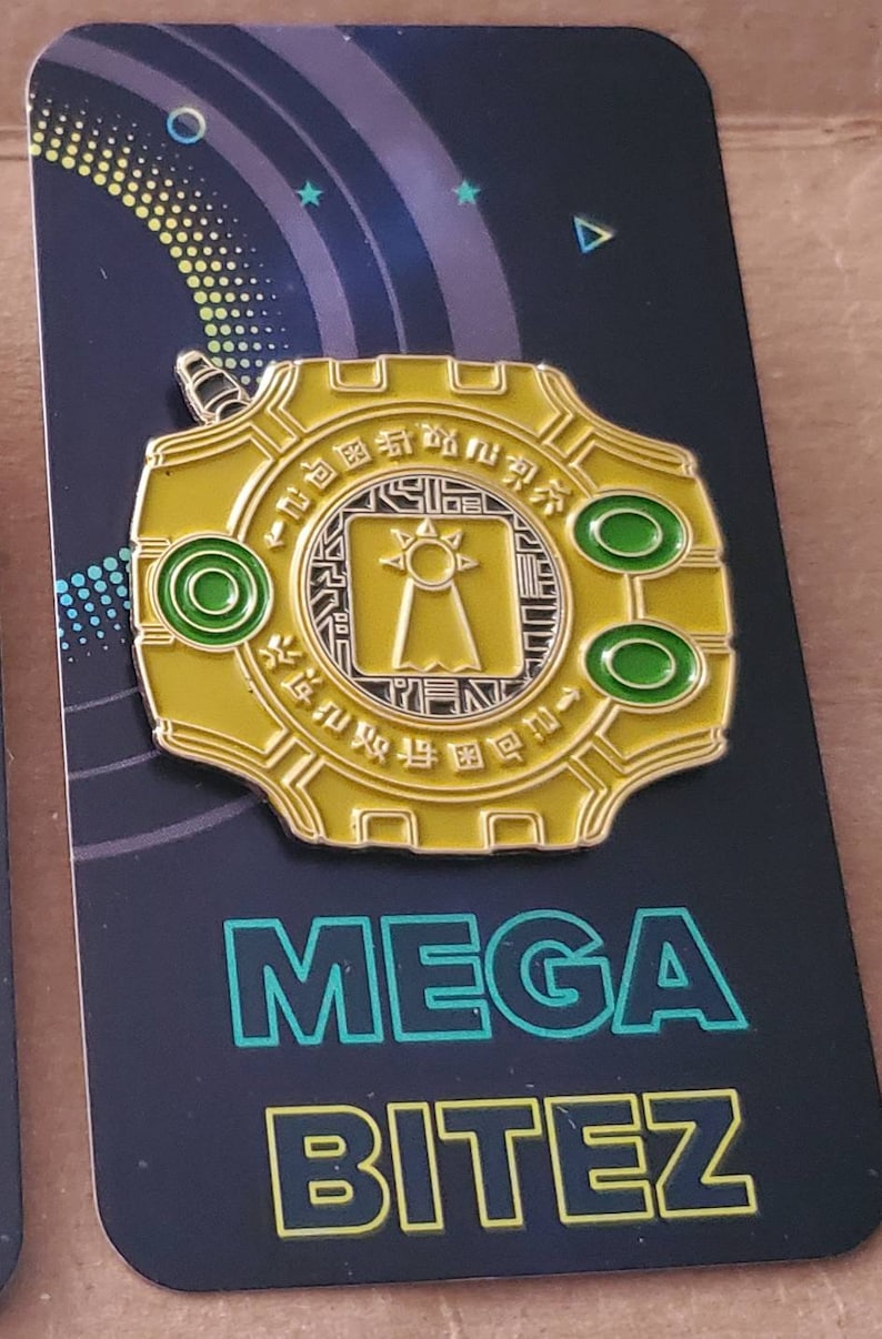 May include: A gold-colored pin with a circular design featuring a black and white symbol with a sun and a tower. The pin has two green circles on the side and the text "MEGA BITEZ" in green and yellow on a black background.