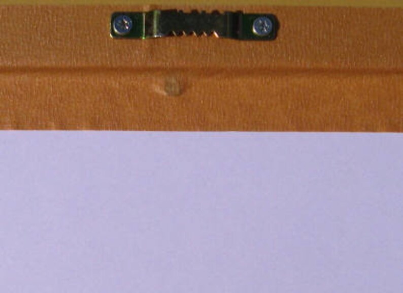May include: A close-up of a brown wooden frame with a metal hanging hook attached to the back. The frame is covered in a light brown paper tape.