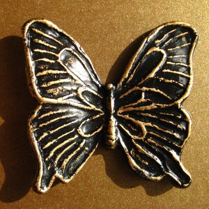 May include: A black and gold butterfly-shaped decorative object with intricate details. The butterfly is made of metal and has a glossy finish.