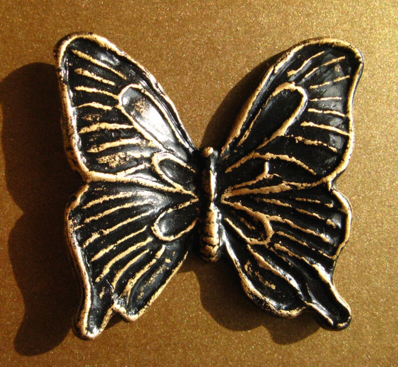 May include: A black and gold butterfly-shaped decorative object with intricate details. The butterfly is made of metal and has a glossy finish.