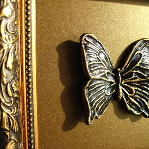 May include: A black metal butterfly ornament with intricate details, mounted on a gold background.