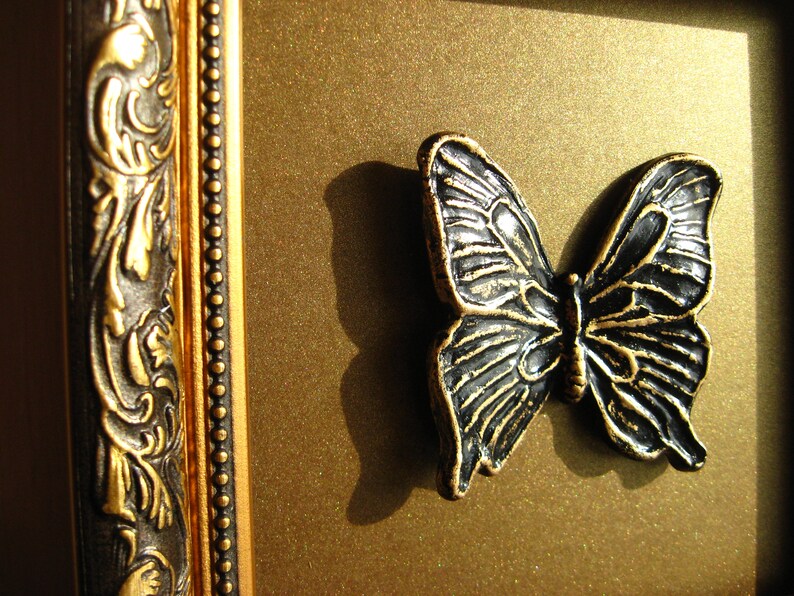 May include: A black metal butterfly ornament with intricate details, mounted on a gold background.
