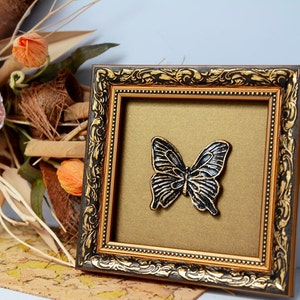 May include: A framed black butterfly wall decor with a gold ornate frame. The butterfly is raised and has a 3D effect.