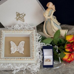 May include: A white box with a gold butterfly design, a white box with a gold design, a blue box with a gold ring, and a bouquet of yellow and red roses.