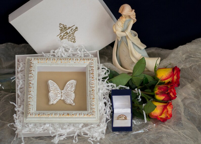 May include: A white box with a gold butterfly design, a white box with a gold design, a blue box with a gold ring, and a bouquet of yellow and red roses.