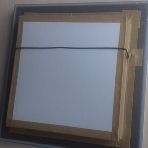 May include: The back of a framed picture with a white mat and brown tape around the edges. A black string is attached to the frame for hanging.