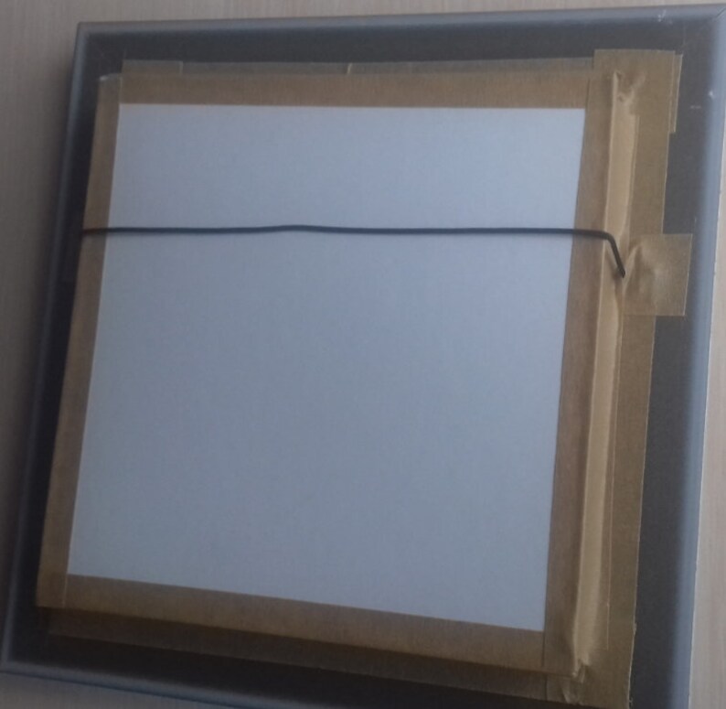 May include: The back of a framed picture with a white mat and brown tape around the edges. A black string is attached to the frame for hanging.
