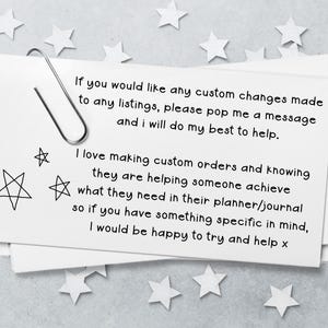 May include: A white rectangular card with a silver paperclip attached to the top left corner. The card features black printed text regarding custom orders and planner assistance, accompanied by three hand-drawn star illustrations on the left side.
