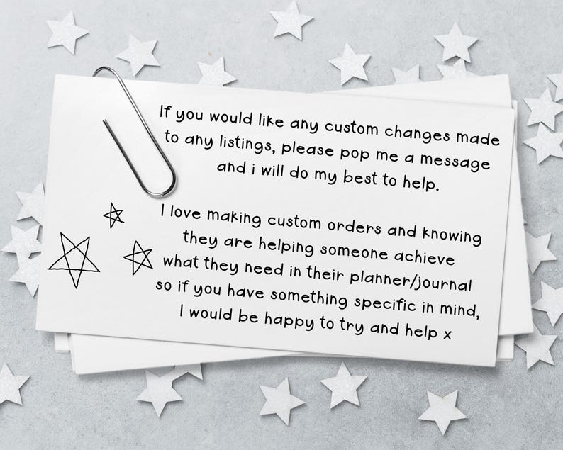 May include: A white rectangular card with a silver paperclip attached to the top left corner. The card features black printed text regarding custom orders and planner assistance, accompanied by three hand-drawn star illustrations on the left side.