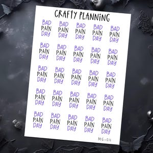 K&ouml;nnte beinhalten: Ein Bogen mit Planer-Aufklebern mit dem Text "BAD PAIN DAY" in Schwarz und Lila. Die Aufkleber sind in Reihen und Spalten angeordnet, wobei die W&ouml;rter vertikal gestapelt sind. Das Blatt ist oben mit "Crafty Planning" und unten mit "MS-011" beschriftet.