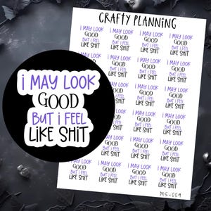 Puede incluir: Una pegatina negra con el texto "I MAY LOOK GOOD BUT I FEEL LIKE SHIT" en letras blancas y moradas. Tambi&eacute;n se ve una hoja de pegatinas con el mismo texto. Las pegatinas son para planificar y hacer manualidades.