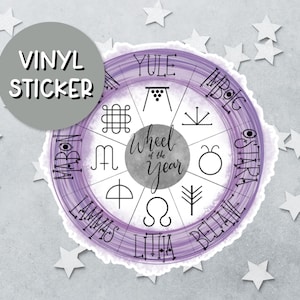 May include: A circular vinyl sticker featuring a purple watercolor-style Wheel of the Year design. The center text reads Wheel of the Year, surrounded by eight segments containing black symbols and the names Yule, Imbolc, Ostara, Beltane, Litha, Lammas, Mabon, and Samhain.