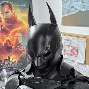 May include: A black Batman costume, featuring a cowl with pointed ears and a detailed chest plate. The costume has a textured appearance and is designed to resemble the character's iconic look. The image is a close-up, showcasing the suit's intricate design.