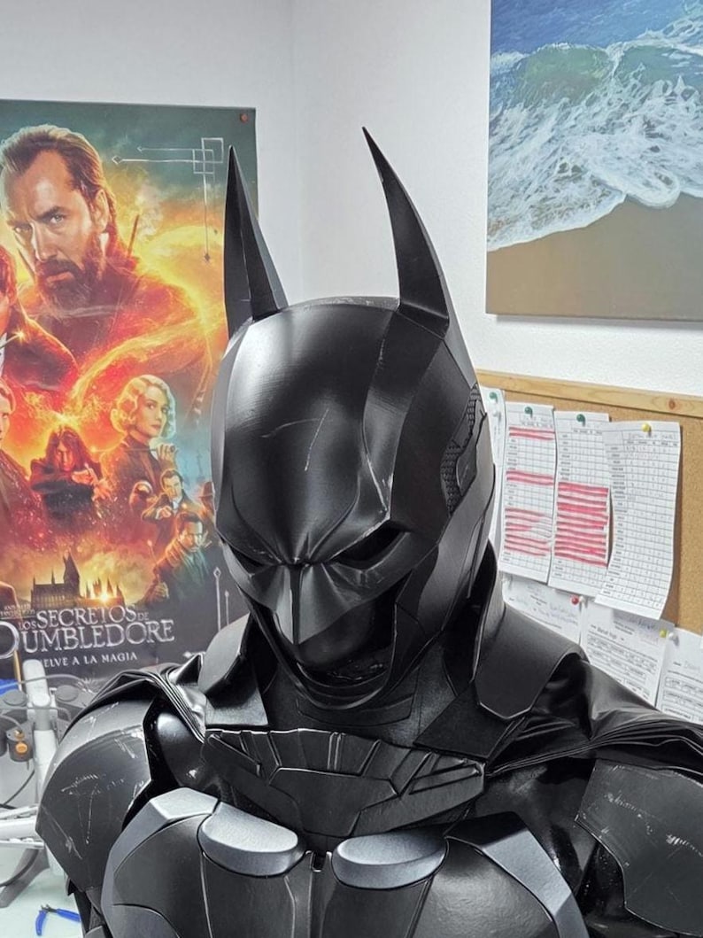 May include: A black Batman costume, featuring a cowl with pointed ears and a detailed chest plate. The costume has a textured appearance and is designed to resemble the character's iconic look. The image is a close-up, showcasing the suit's intricate design.