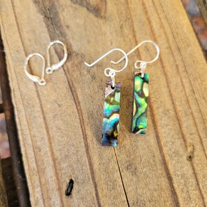 May include: A pair of silver earrings with iridescent abalone shell rectangular pendants. The earrings have a hook closure.
