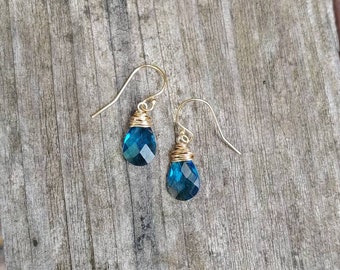Puede incluir: Un par de pendientes de alambre dorado envueltos con piedras de topacio azul en forma de lágrima.