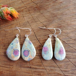 May include: A pair of teardrop-shaped earrings with a light blue and white base and pink accents. The earrings are made of a natural stone and have silver hooks.